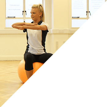 Instructor stretching arms whilst on gym ball